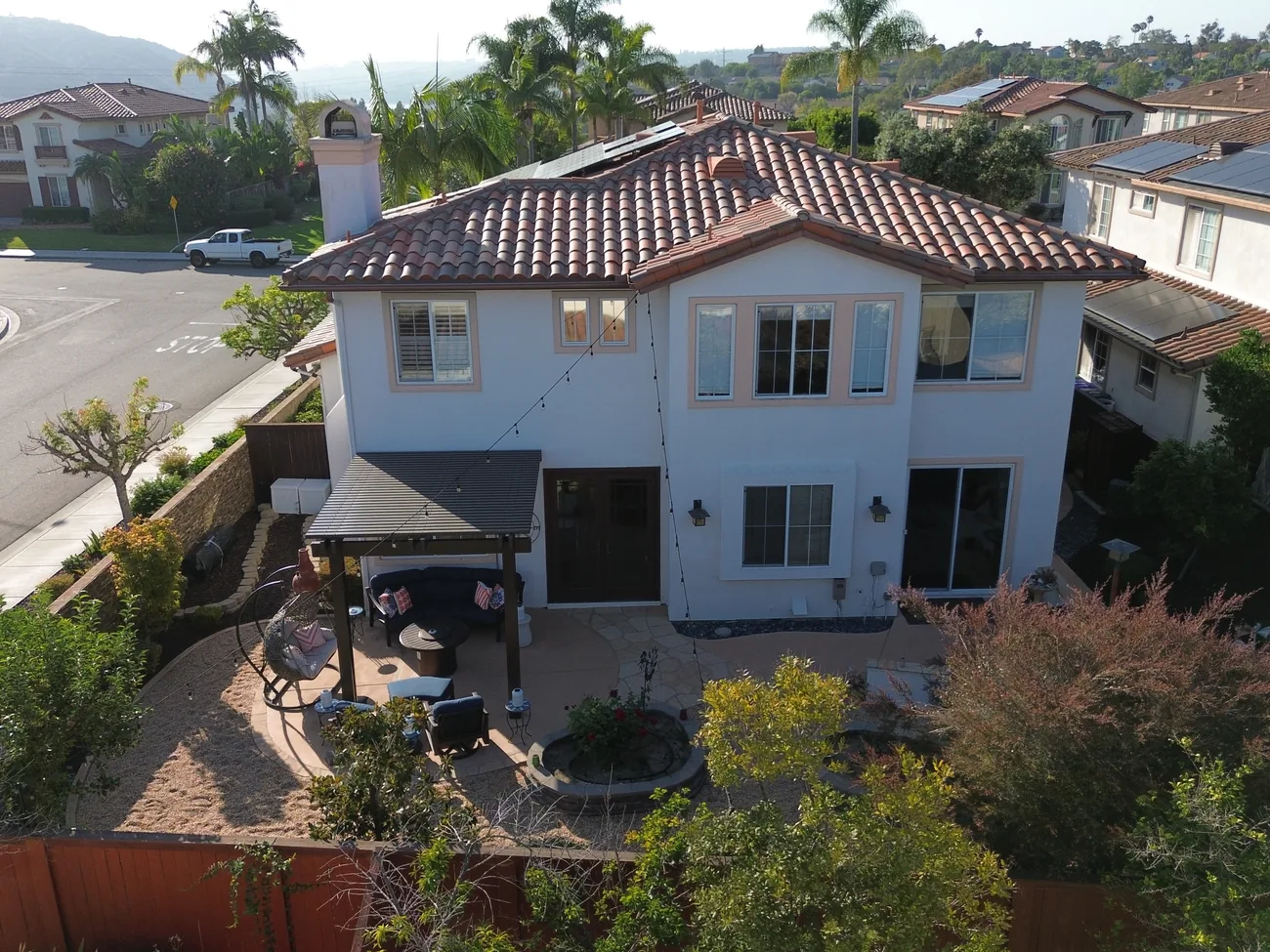 Aerial view of the covered backyard patio, pergola with string lights, and lounge seating at 2193 Vista La Nisa